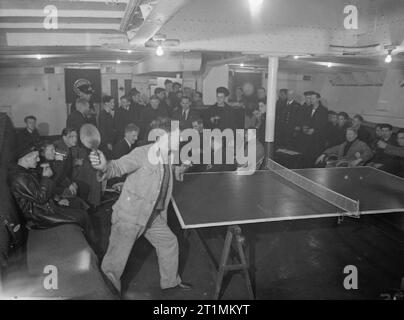 The Royal Navy during the Second World War View of the recreation room on the AUTOCARRIER. A large group of sailirs sit around chatting or sharing a joke. In the foreground a sailor has just returned a serve in a table tennis game. In the recreation room the men can play table tennis, darts, cards, or for the musical, have a sing-song round the piano. Stock Photo