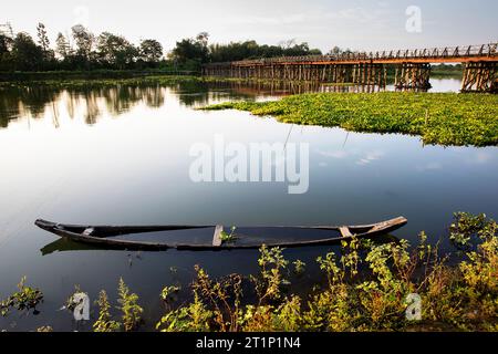 Side view of a wooden bridge over a river and a typical wooden boat half submerged in the water on Majuli island, Assam, India Stock Photo