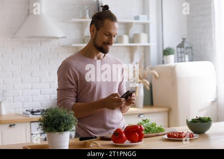Positive young homeowner man using smartphone in kitchen Stock Photo