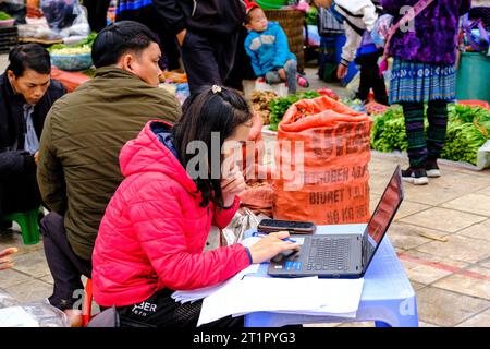 Bac Ha, Vietnam.  Sunday Market Scene, Young Woman Working on Laptop Computer. Lao Cai Province. Stock Photo