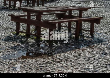 Deserted picnic table on rain soaked cobblestones after a rain shower. Stock Photo