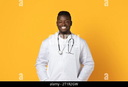 Cheerful black man doctor in white coat on yellow background Stock Photo