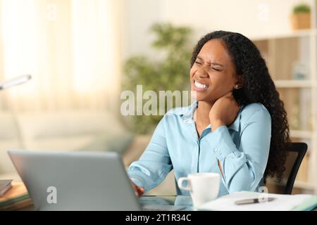 Black teleworker suffering neck ache sitting on a chair at home Stock Photo