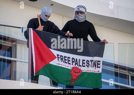 Los Angeles, USA. 14th Oct, 2023. Two supporters of Palestine display a flag from a balcony across from the Israeli Consulate in Los Angeles. Credit: Sipa USA/Alamy Live News Stock Photo