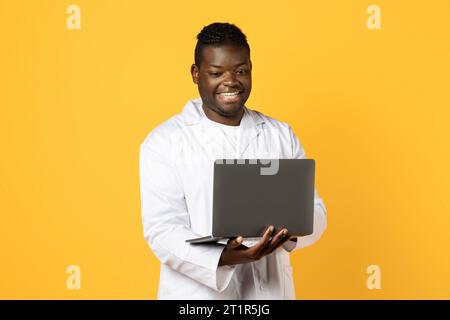 African american man doctor working on laptop over yellow background Stock Photo