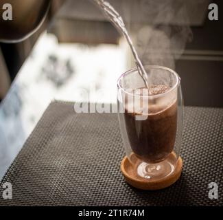 Shot of the hot water being poured into the transparent cup to brew the coffee. Stock Photo