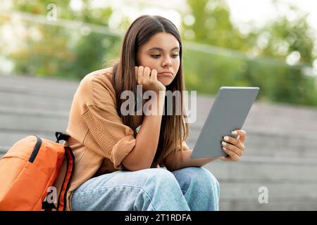Upset young woman student using digital tablet outdoors Stock Photo