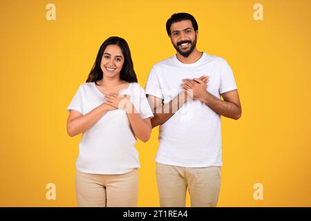 Couple placing hands on heart, yellow background Stock Photo
