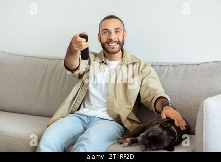 Happy millennial man having rest, switching channels with remote controller Stock Photo