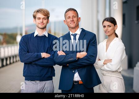 Three business professionals standing in front of a modern office building, each with arms crossed in a confident pose Stock Photo