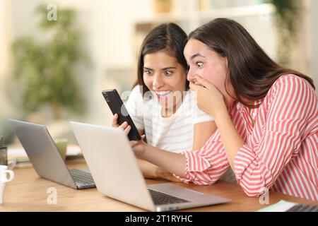 Two amazed tele workers checking phone content at home Stock Photo