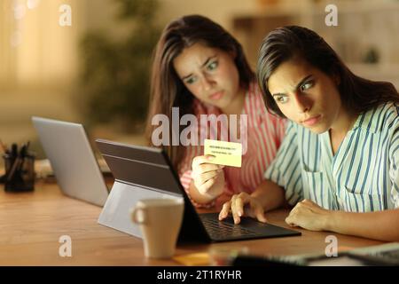 Two suspicious tele workers buying online with credit card and laptops in the night at home Stock Photo