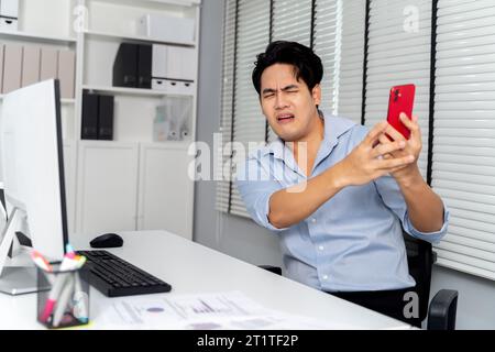 Angry Asian business man being yelled , scolded, complained on the mobile phone for in the office room setting. - Business fight and conflict at workplace concept Stock Photo