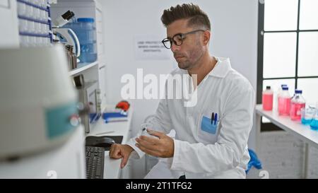 Attractive young hispanic man, working tirelessly in the lab, engrossed scientist holding a test tube, fixated on computer screens while experimenting Stock Photo