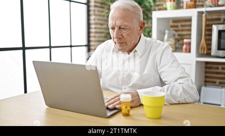 Senior grey-haired man having online medical consultation holding pills at dinning room Stock Photo