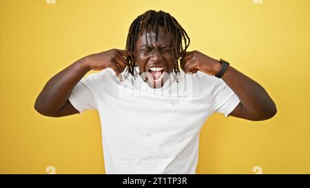 African american man screaming loudly covering ears with fingers over isolated yellow background Stock Photo