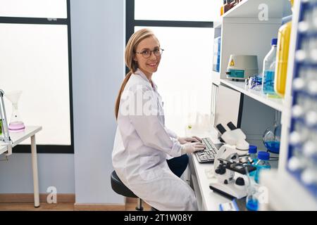 Young blonde woman scientist smiling confident using computer at laboratory Stock Photo