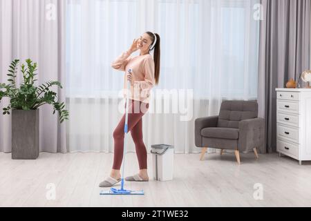 Enjoying cleaning. Happy woman in headphones listening music and mopping at home Stock Photo