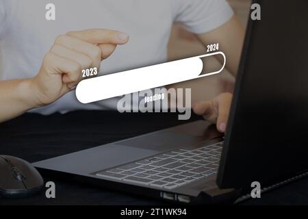 A woman's hand presses a virtual button on a long button with the inscription loading from 2023 to 2024, working on a laptop at the table, Happy New Y Stock Photo