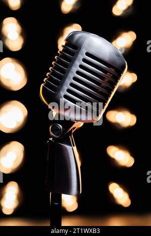 Close up of vintage microphone on stand in dark studio. Podcast old microphone with blurred light bulbs on black background. Concept of podcasting, event. Stock Photo