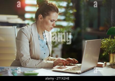 sad modern 40 years old business woman in a light business suit in modern green office with laptop. Stock Photo