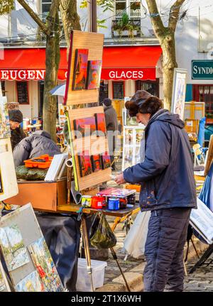 A male artist at work painting pictures on canvas on an easel outdoors  in Place du Tertre, Montmartre, 18th arrondissement, Paris, France Stock Photo