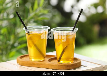 Plastic cups of tasty iced tea with lemon on white wooden table against blurred background Stock Photo