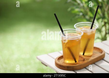 Plastic cups of tasty iced tea with lemon on white wooden table against blurred background, space for text Stock Photo