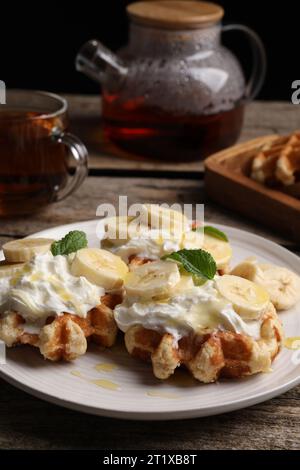 Delicious Belgian waffles with banana and whipped cream served on wooden table Stock Photo