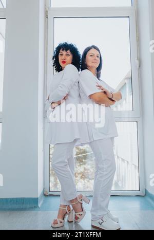 Female Specialist and Doctor Posing Back to Back in Hospital Hallway Stock Photo