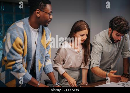 Multiracial executives discuss blueprints in a collaborative boardroom meeting, showcasing cross-generational teamwork in a multinational office. Stock Photo