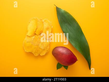 Sweet dried large mango slices on yellow background with raw fruit and leaf.Top view. Stock Photo
