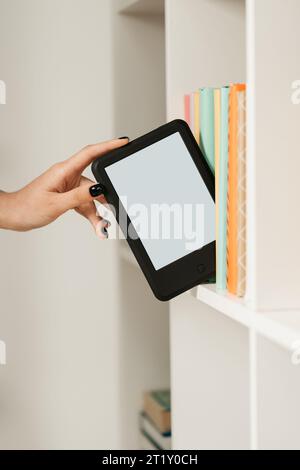 Man taking modern e-book reader from a bookshelf close up Stock Photo