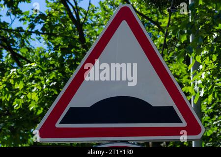 Triangular warning road sign Hump in the road beautiful blue cloudy sky. Stock Photo