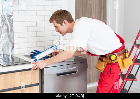 Gloved craftsman installs hob in kitchen. Household Appliance Installation Services Concept Stock Photo