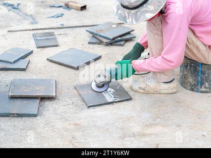 Worker grinding steel plate, man using grinder to work on piece of metal in workshop. Stock Photo