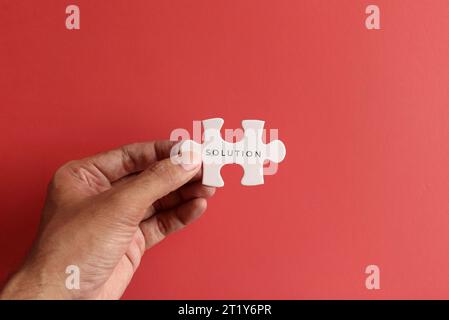 Hand holding puzzle pieces with text SOLUTION on red background. Stock Photo