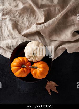 Festive autumn table setting with pumpkins in a black plate with tablecloth over black background. Top view. Stock Photo