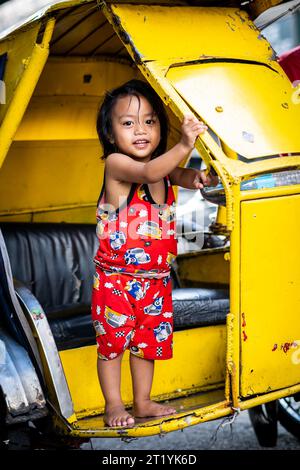 A cute Filipino girl plays on her fathers tricycle, pedicab or rickshaw in Ermita, Manila, Philippines. Stock Photo