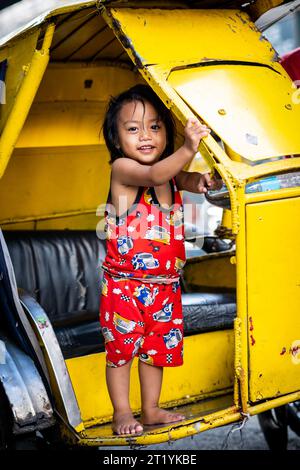 A cute Filipino girl plays on her fathers tricycle, pedicab or rickshaw in Ermita, Manila, Philippines. Stock Photo