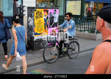 A Paris street scene a man on a bicycle stopped an a crossing near Hôtel de Ville with a dachshund in the handlebar basket, people, posters, street s. Stock Photo