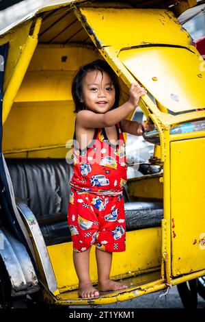 A cute Filipino girl plays on her fathers tricycle, pedicab or rickshaw in Ermita, Manila, Philippines. Stock Photo