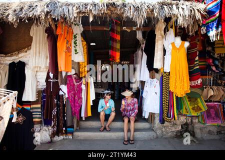 Two young women enjoy ice cream sandwiches on the steps of a clothing shop in Todos Santos, Baja California Sur, Mexico. Stock Photo