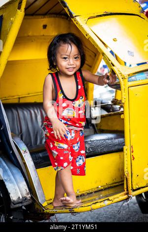 A cute Filipino girl plays on her fathers tricycle, pedicab or rickshaw in Ermita, Manila, Philippines. Stock Photo