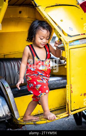 A cute Filipino girl plays on her fathers tricycle, pedicab or rickshaw in Ermita, Manila, Philippines. Stock Photo