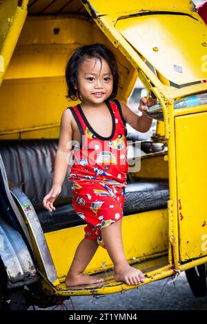 A cute Filipino girl plays on her fathers tricycle, pedicab or rickshaw in Ermita, Manila, Philippines. Stock Photo