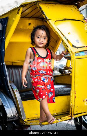 A cute Filipino girl plays on her fathers tricycle, pedicab or rickshaw in Ermita, Manila, Philippines. Stock Photo