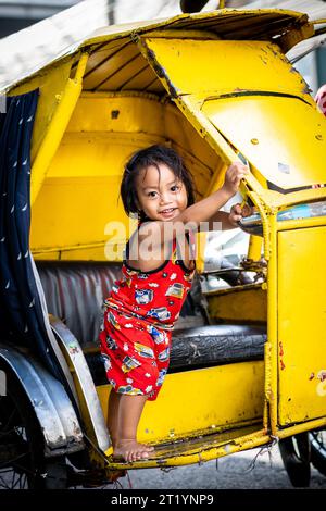 A cute Filipino girl plays on her fathers tricycle, pedicab or rickshaw in Ermita, Manila, Philippines. Stock Photo