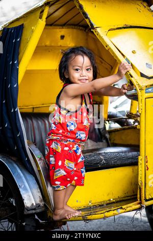 A cute Filipino girl plays on her fathers tricycle, pedicab or rickshaw in Ermita, Manila, Philippines. Stock Photo