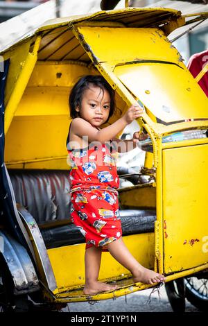 A cute Filipino girl plays on her fathers tricycle, pedicab or rickshaw in Ermita, Manila, Philippines. Stock Photo